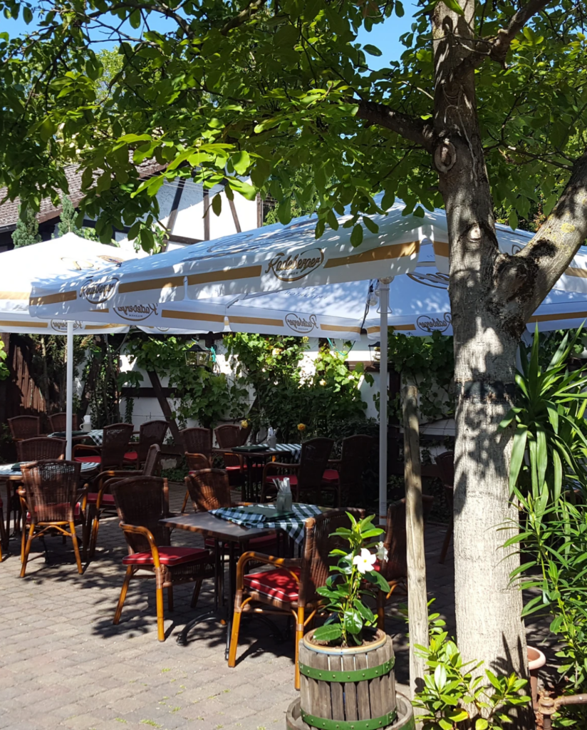 Gemütliche Außenterrasse des Restaurants mit Schirmen, umgeben von Grün und komfortablen Sitzgelegenheiten für ein entspanntes Esserlebnis im Restaurant "Altes Holztor" in Eltville am Rhein.